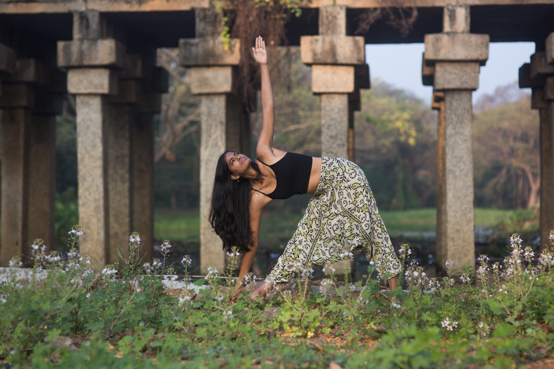 Sneha in a triangle yoga pose by stone pillars